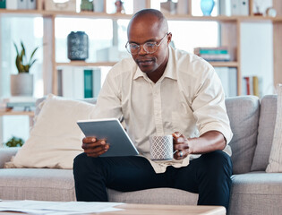 Tablet, coffee and relax with a black man on the sofa, sitting in the living room of his home or office. Business, tech and research with a male employee reading an online article while on a break