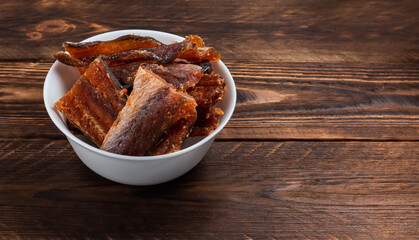 Pieces of cleaned dried fish in the bowl on wooden background. Dry Peppered Pollack. Amber with pepper