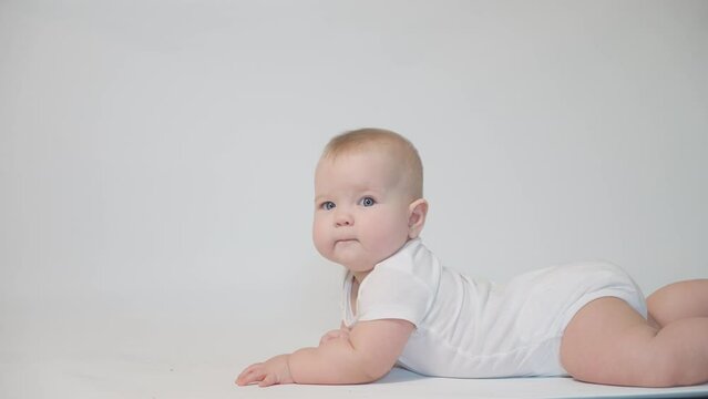 Infant on white background lying on his belly looking at the camera