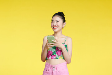 Relaxed pretty woman in crop top leaning and smiling while surfing on smartphone on yellow background with garden