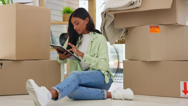 Tablet, boxes and female moving to a house or apartment doing research for her space. Technology, relax and young woman planning her modern new home on the internet while sitting on the floor.