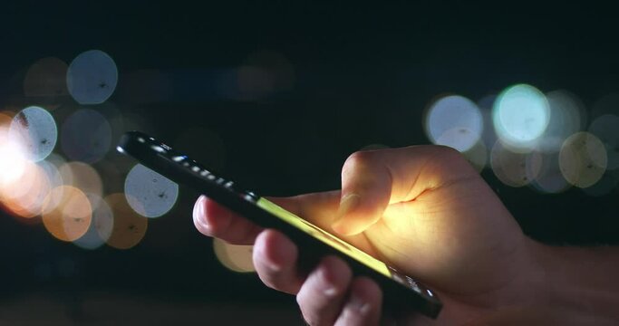 Close-up of person using smartphone, browsing through pictures on social network wall at night. Male finger scrolling social media app feed on smartphone on night city background, close up macro shot.