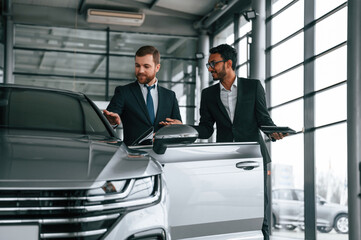 Standing and talking near automobile. Man is consulting the customer in the car showroom