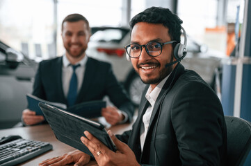 Using modern technology, graphic tablet, pc. Two businessmen are working together in the car showroom