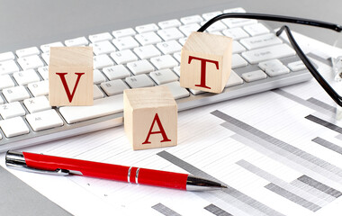 Fototapeta premium VAT written on a wooden cube on the keyboard with chart on grey background