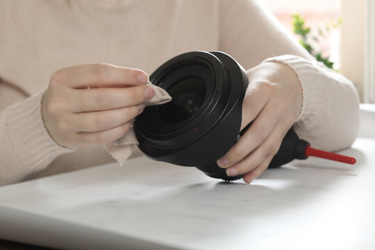 female photographer cleaning dslr fisheye camera lens with microfiber cloth, wipes dust of camera lens