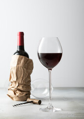 Bottle of wine in shopping paper bag with opener and glass of wine on light background.