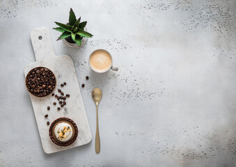 Coffee cup with raw beans and golden spoon and caramell dessert on marble board.