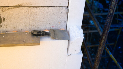 An old spatula lies on the foam glued to the wall of the house. Insulation of a house with walls made of aerated concrete bricks with polystyrene foam
