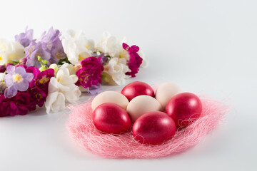 Obraz na płótnie Canvas pink nest with bright pink easter eggs and colorful spring flowers on a white background. easter decor. selective focus