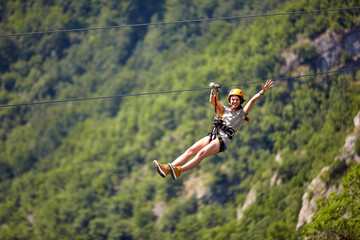 Happy young cheerful female tourist wearing casual clothes riding on zipline in forest.  Zipline...