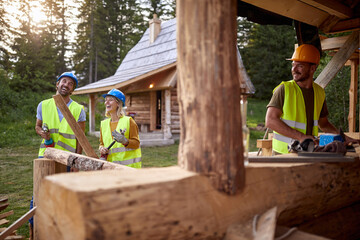 Builders are in a good mood while working at the cottage construction site in the forest. Workers,...