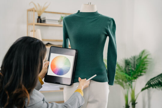Female fashion designers design a product using a laptop computer with a digital tablet in a modern studio in the morning.