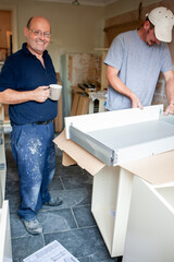 Kitchen Fitters: Working Together. A friendly smile from a worker taking a break while his colleague works on. From a series of related images.