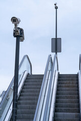The monitoring of security cameras at the top of an outdoor escalator to monitor the safety of citizens