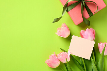 Happy Mothers Day gift with ribbon bow, greeting card template, and tulips on green background. Flat lay, top view, copy space.