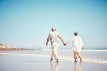 Holding hands, beach and an old couple walking outdoor in summer with blue sky mockup from behind. Love, romance or mock up with a senior man and woman taking a walk on the sand by the ocean or sea - Powered by Adobe