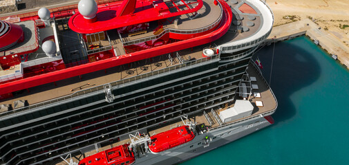 Aerial view of a large cruise ship docked at the port. There is no one on board and the ship is empty. The ship is white with red decorations.