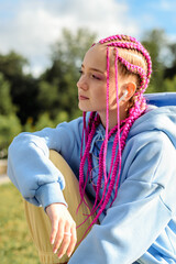 Portrait of a caucasian teenage girl with pink braids using wireless headphones in the park.Technology,summer concept.Generation Z style.