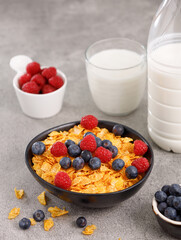 Tasty corn flakes with blueberries and raspberries in a black bowl with milk