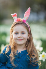 Easter. Little cute girl 5 years old with rabbit ears on the lawn of daffodils. Happy child. Spring holidays.