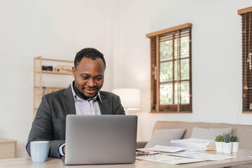 Focused african american businessman working with laptop documents in office holding papers preparing report analyzing work results, black male analyst doing paperwork at workplace using computer