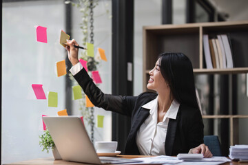 businesswoman write tasks creative ideas and planning on sticky post it note on glass wall.project...