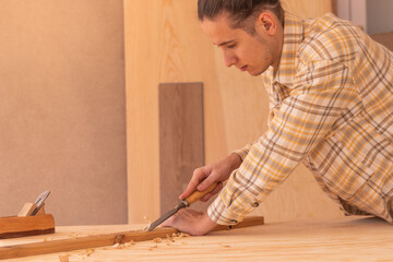 Craftsman gouging wood with chisel. Side view of attentive male woodworker carving wood with rasp near jack plane on workbench