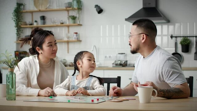 Family Playing Board Game. Happy Asian family with one kid plays board card game with dies sitting at home.