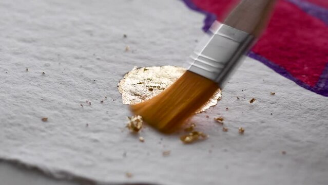 A close up of an artist buffing away gold leaf sheets with brush from artwork to reveal circle sun art with red art in background, with asmr soothing brush sounds audio