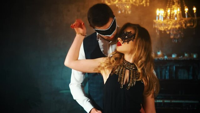 Two person sexy couple posing man and blonde hair woman geddess in carnival mask dancing. Gothic Girl dancer passion moves seduces Black dress. Portrait Guy fantasy Fashion model. dark party room 4k