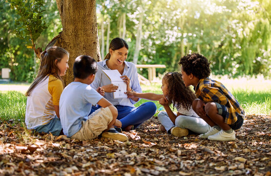 Books, reading or teacher with children in a park storytelling for learning development or growth. Smile, tree or happy educator with stories for education at a kids kindergarten school in nature