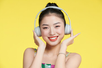 happy young woman adjusting headphones while listening music isolated on pink