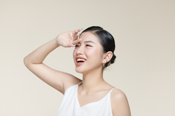 Fototapeta premium Young asian woman covers her face from the sun with palm against a beige background