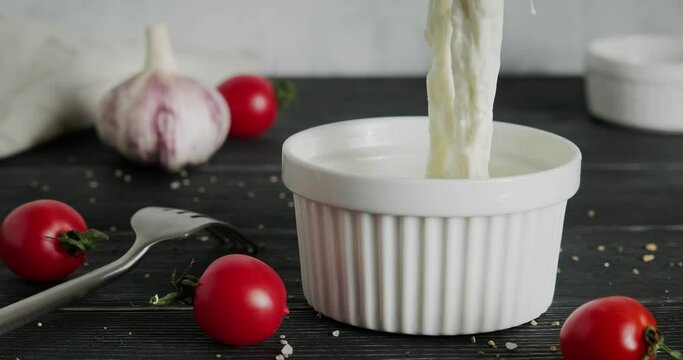 Pullling stracciatella cheese out of bowl with fork. Italian mozzarella cheese shreds soaked in milk, Italian curd cheese, close up video clip, side view high quality 4k footage