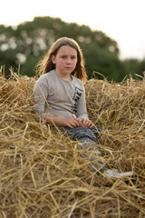 Naklejka na ściany i meble Sad pensive girl sitting on a haystack