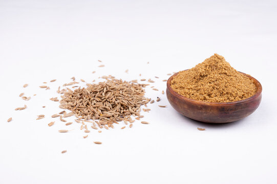 cumin seeds and cumin ground, powder. Pile of cumin powder isolated in a rock bowl on white background. Heap of ground caraway. Selective focus. Top view.
