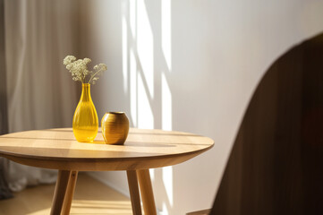 Cozy home interior. Beige wooden table with yellow vase in the sunlight. Apartments background with space for text