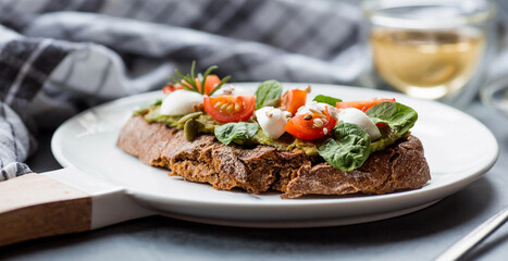 Bruschetta (sandwiches) with cherry tomatoes, mozzarella cheese and herbs on a stylish plate on a dark background. A traditional Italian snack.