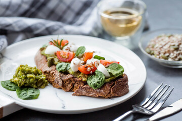 Bruschetta (sandwiches) with cherry tomatoes, mozzarella cheese and herbs on a stylish plate on a dark background. A traditional Italian snack.