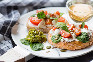 Bruschetta (sandwiches) with cherry tomatoes, mozzarella cheese and herbs on a stylish plate on a dark background. A traditional Italian snack.