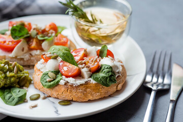 Bruschetta (sandwiches) with cherry tomatoes, mozzarella cheese and herbs on a stylish plate on a dark background. A traditional Italian snack.