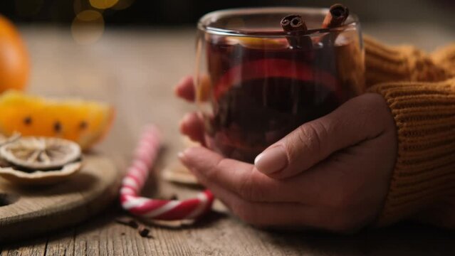 Woman holding transparent glass with mulled wine and cinnamon sticks