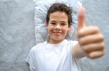 Top view of happy little boy lying on the floor with thumbs up
