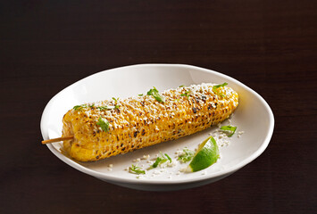 Elote (Spanish Corn) in a white plate with a slice of lime on a dark wooden surface; copy space