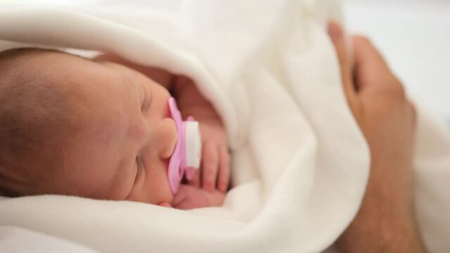 Adorable newborn baby sleeping on his father hands. Closeup view of infant child swaddled in blanket napping on his parent cheast at home