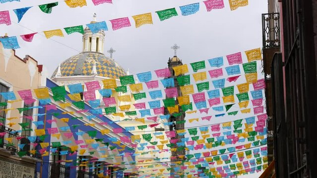 Church of San Cristóbal with colorful mexican perforated papel picado banner, festival colourful paper garland. Multi colored hispanic folk carved tissue flags, holiday or carnival.