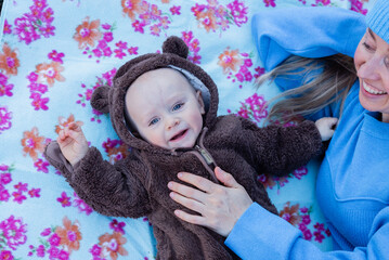 Smiling young woman looking to her happy baby boy in teddy bear jumpsuit.