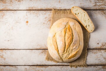loaf of bread, freshly baked bread sliced into slices, freshly baked bread on top of a kitchen towel on a wooden table