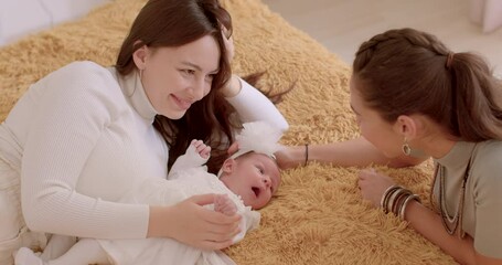 Two young women look at a newborn, talking, smiling. Baby's first days at home. Couple has won the right to adopt a child.